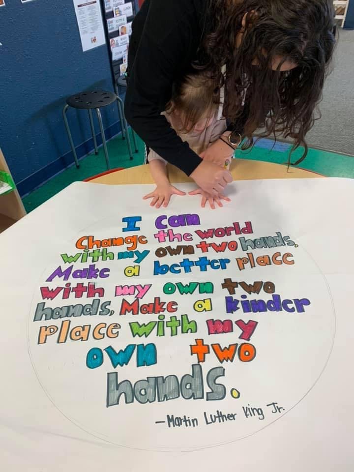 Person and child with hands on a poster with text about changing the world