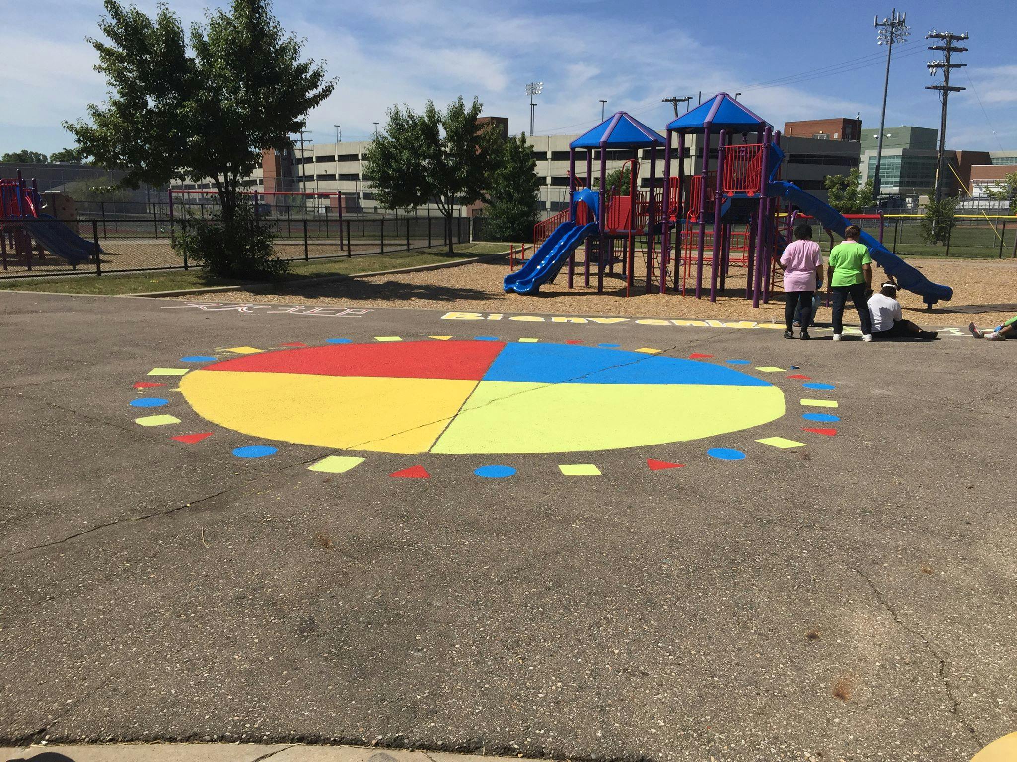 People painting a colorful circle on asphalt near a playground