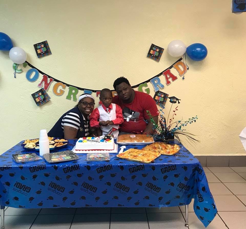 Three people posing behind a table with a cake and food, with "CONGRATS GRAD" banner