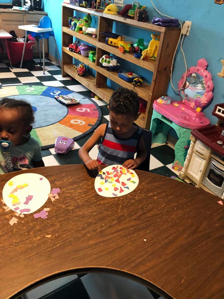 Child doing craft at a table with another child nearby