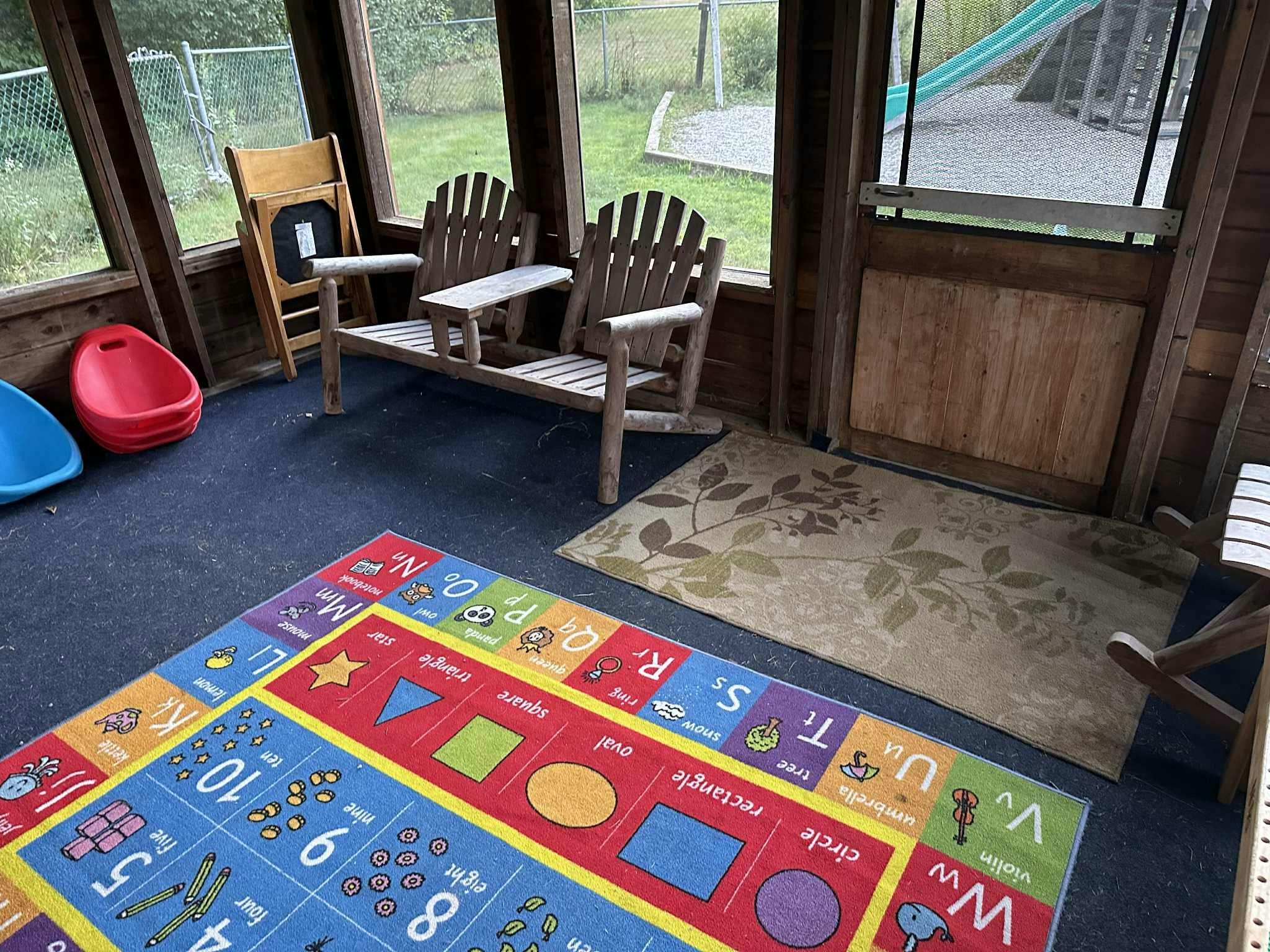 Sunroom with a colorful alphabet rug, two Adirondack chairs, and small plastic chairs