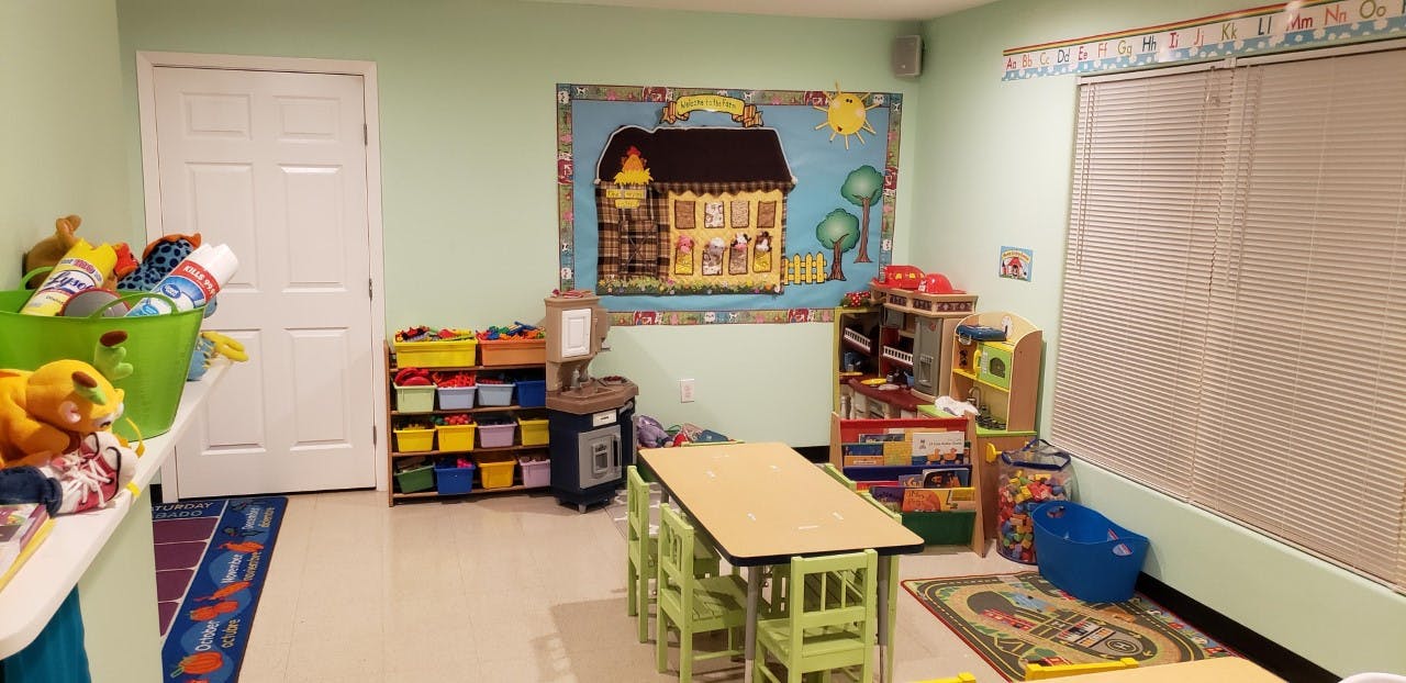 Classroom with small tables and chairs, storage shelves, and a house-shaped bulletin board