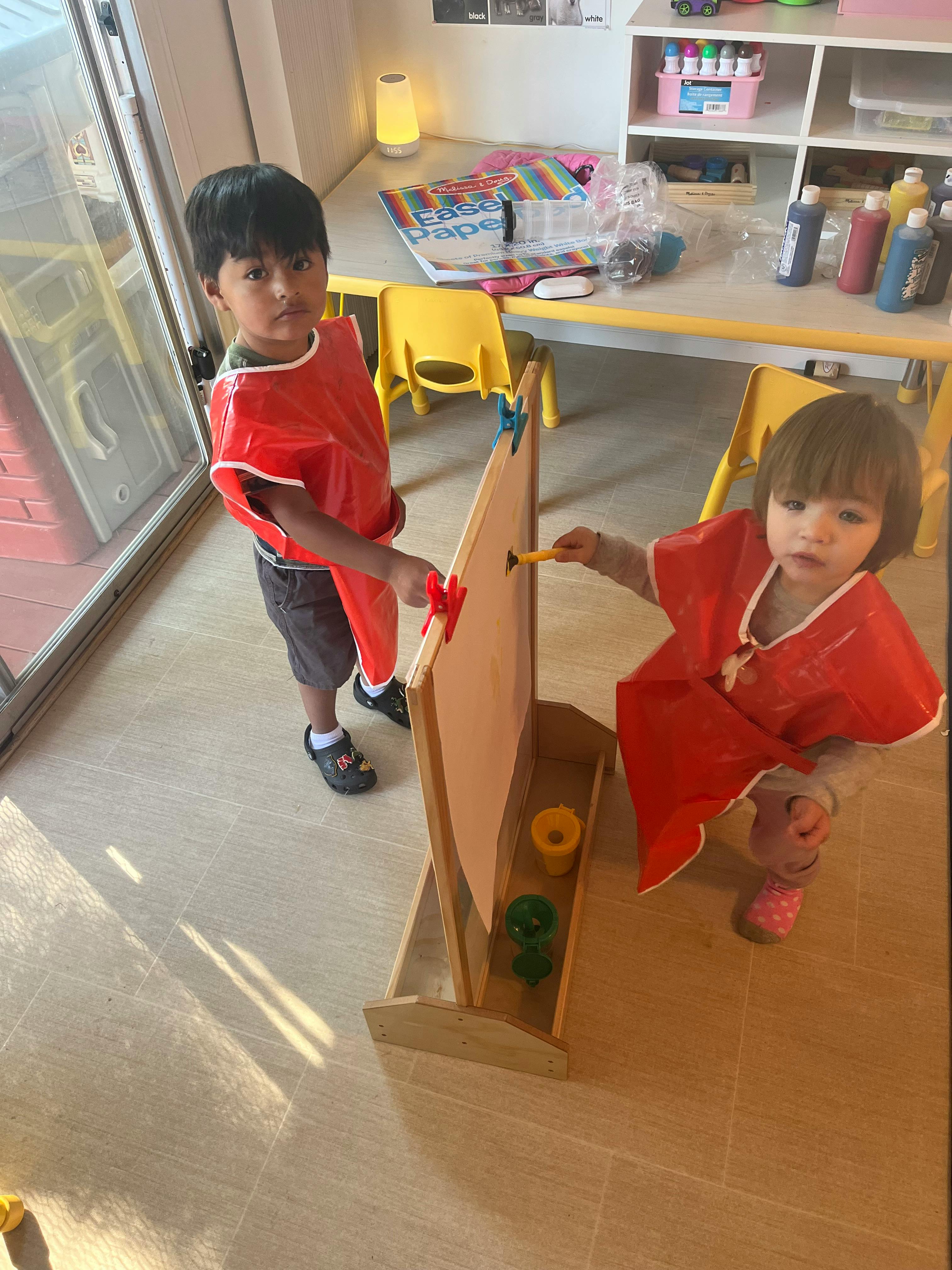 Two children painting on an easel