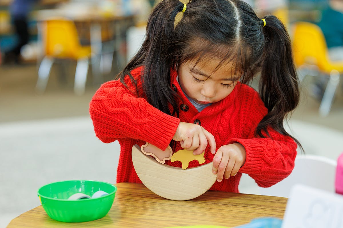 Child playing with wooden shapes in a bowl