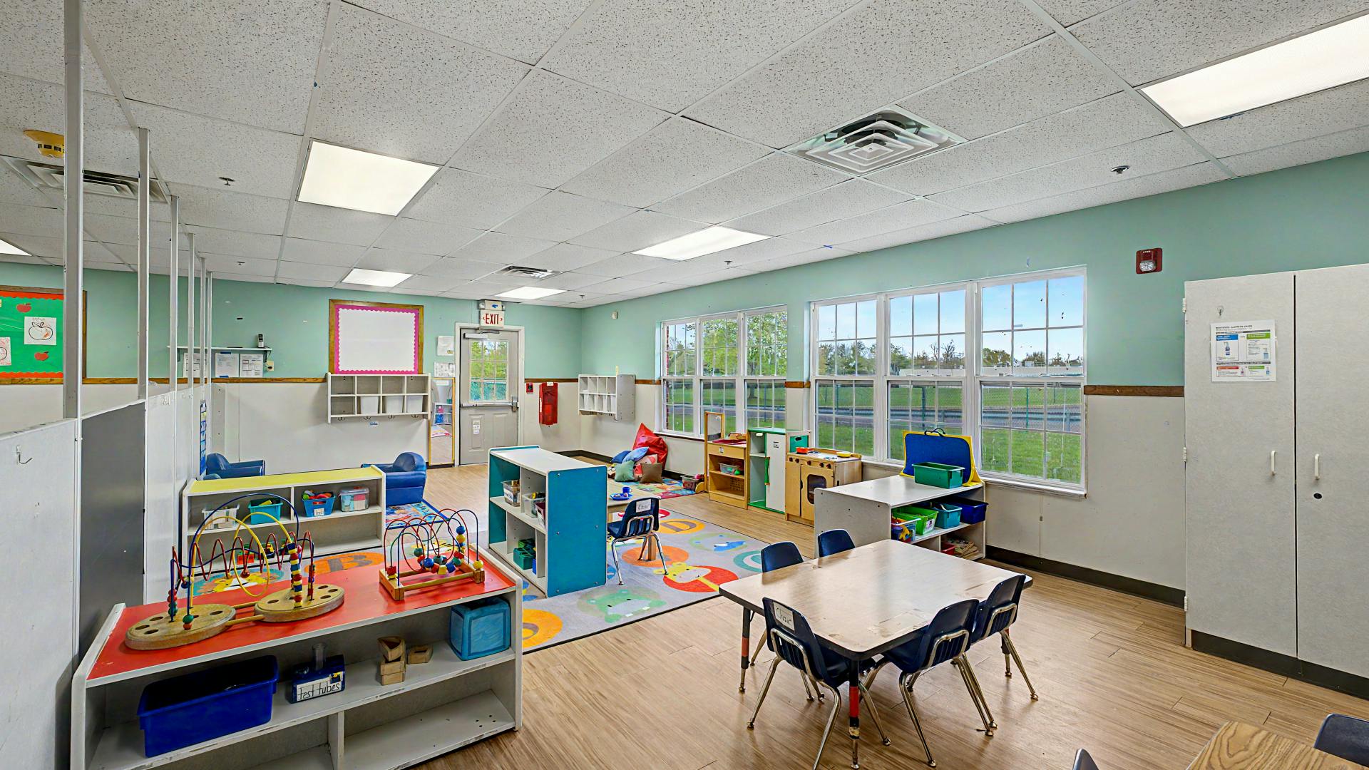 Classroom with child-sized tables and chairs, play mats, and toys