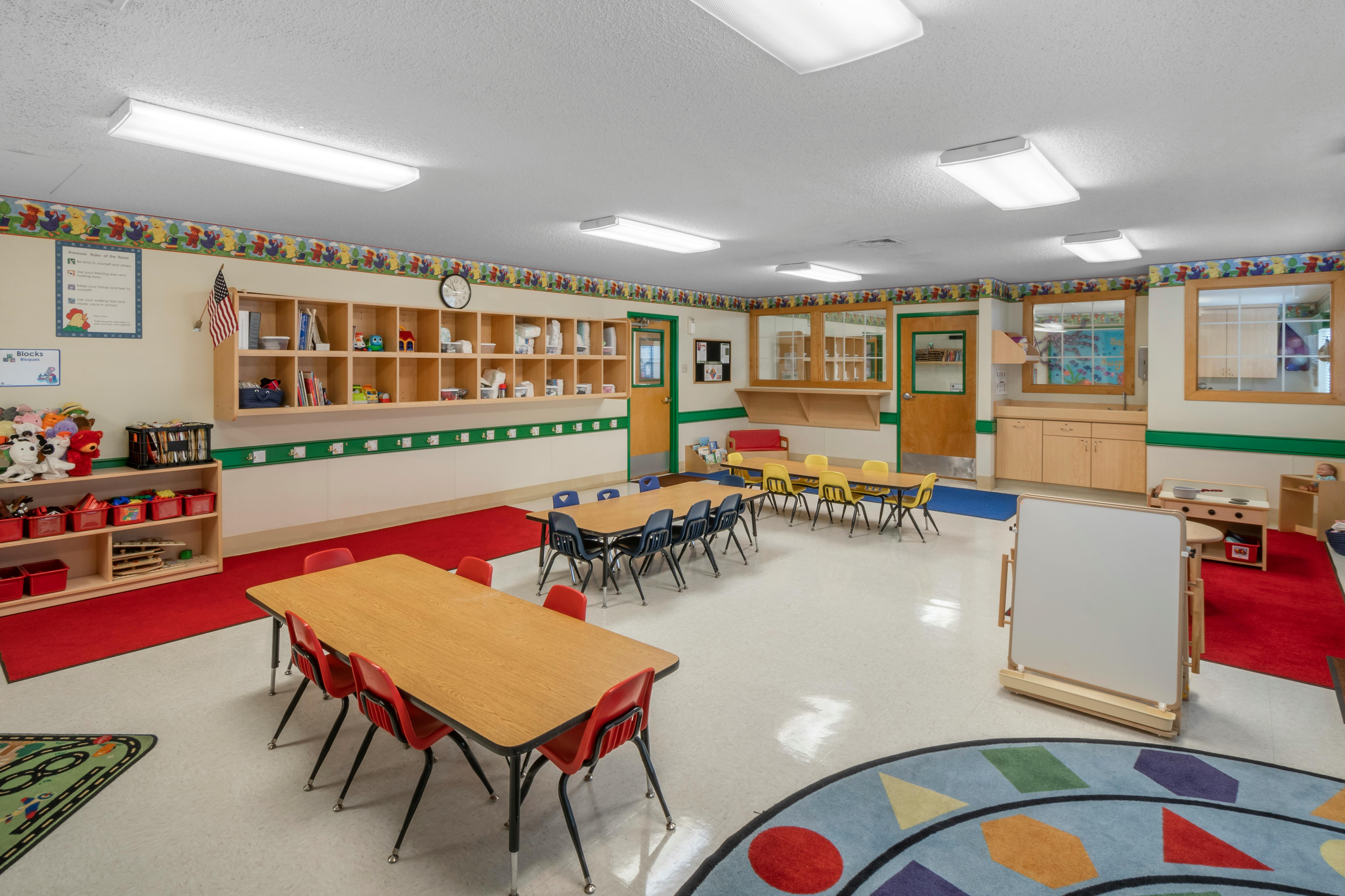 Classroom with child-sized tables and chairs, shelves, and colorful rugs
