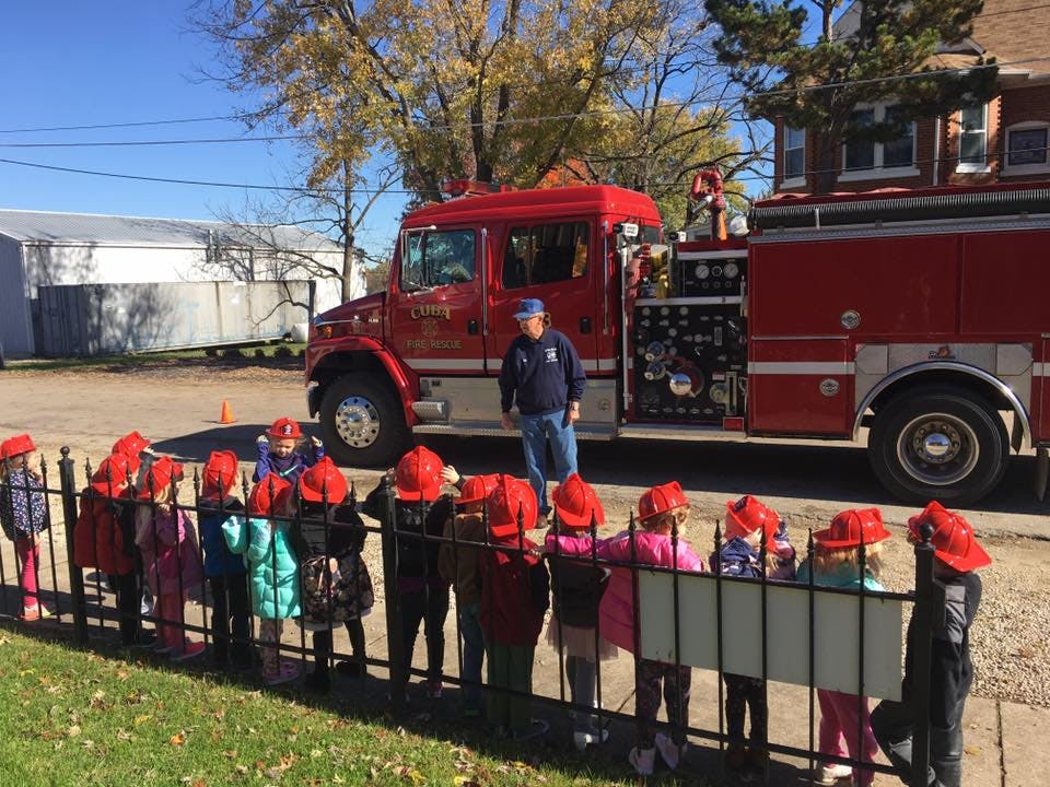 Children in red hats looking at a person next to a fire truck