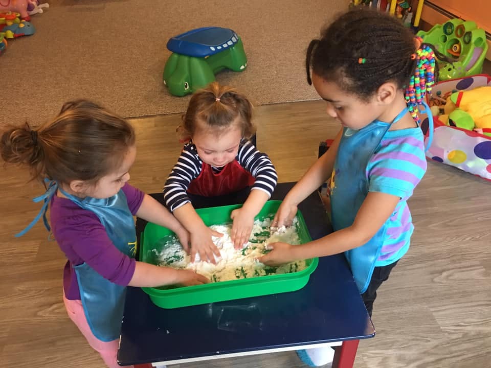 Three children playing with a sensory bin in a classroom
