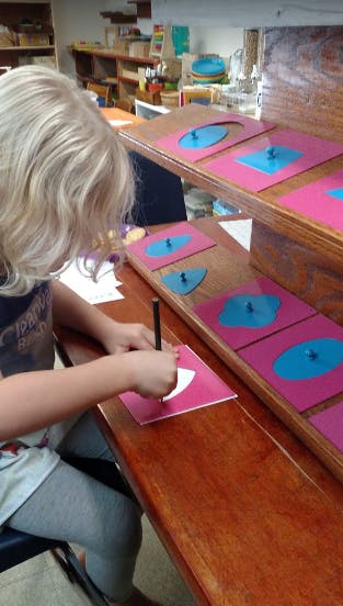 Child tracing a shape on a pink card with a pencil