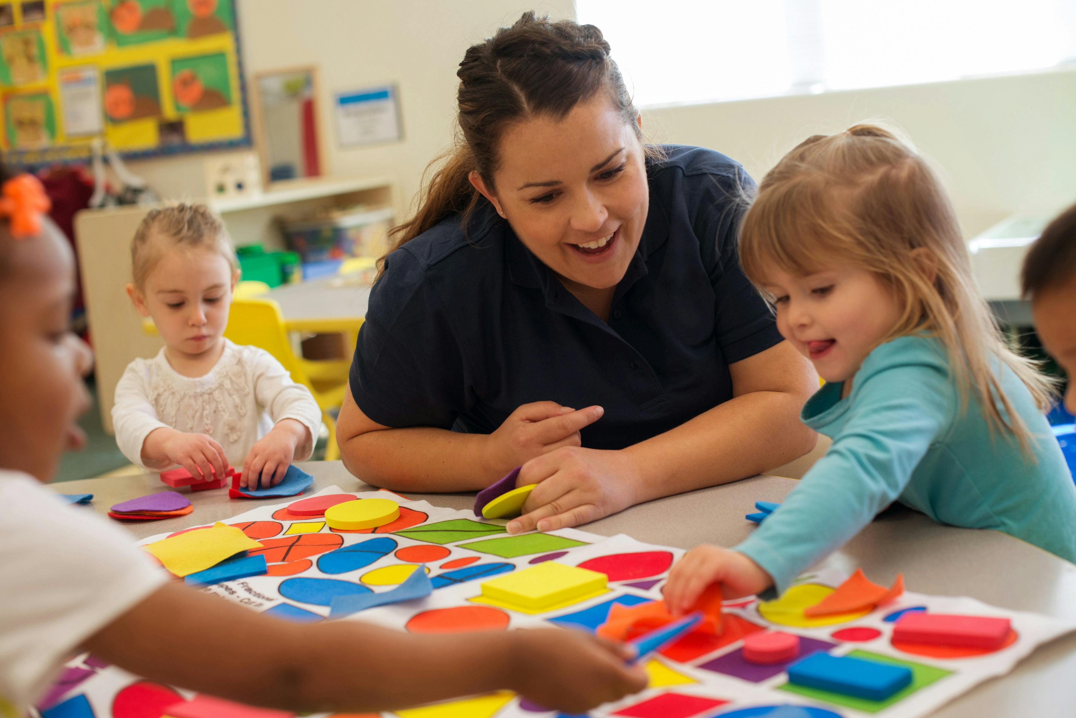 Adult and children playing with colorful shapes on a table in a classroom
