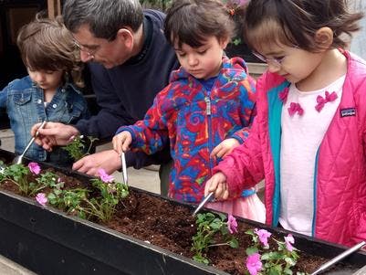 Adult and three children planting flowers in a planter box