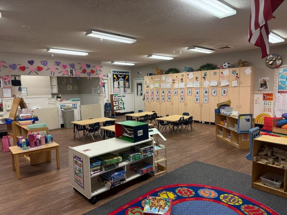 An empty classroom with tables, chairs, storage cabinets, and decorations