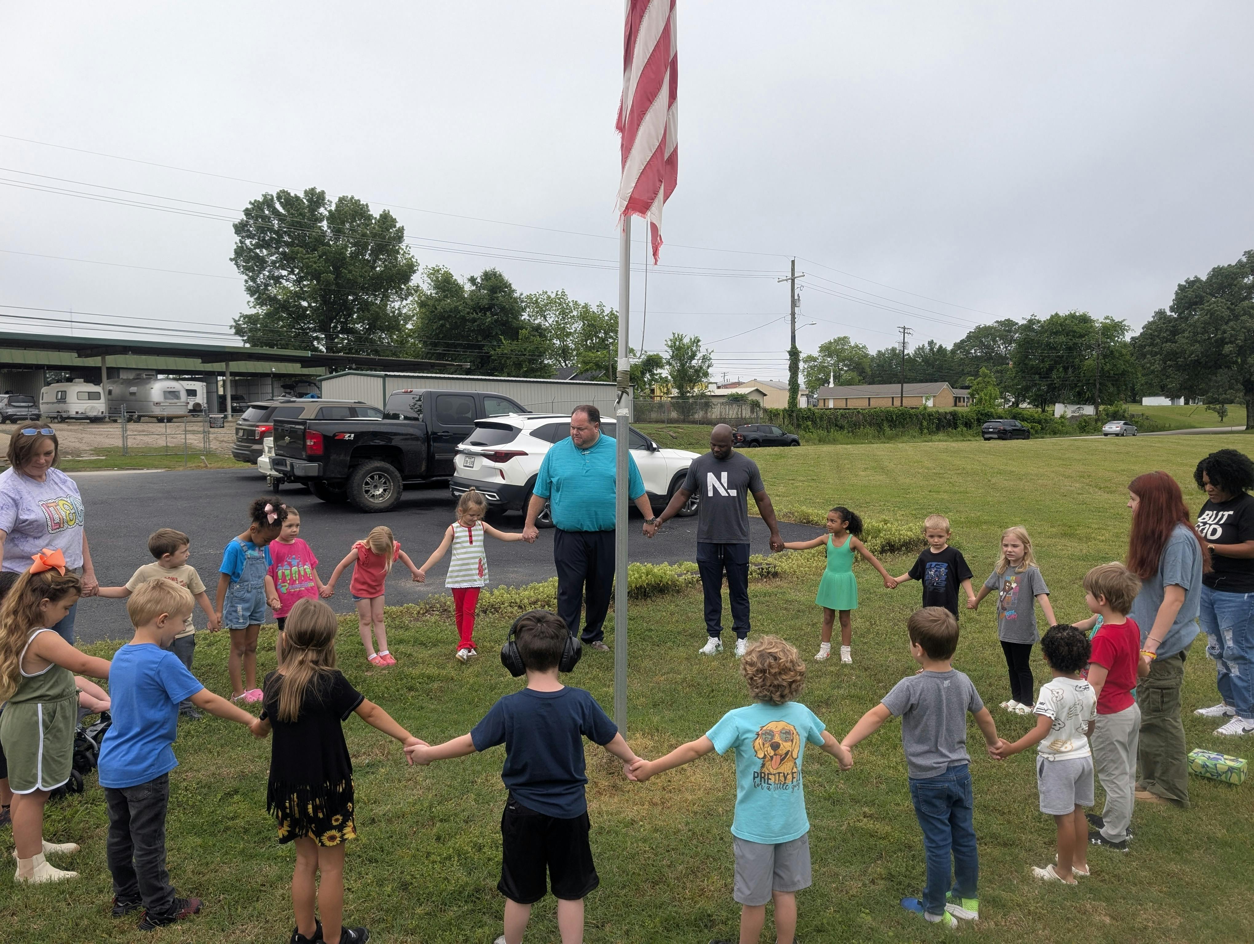 People and children holding hands in a circle around a flagpole