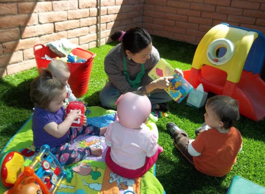 Person reading a book to three children on a mat outdoors