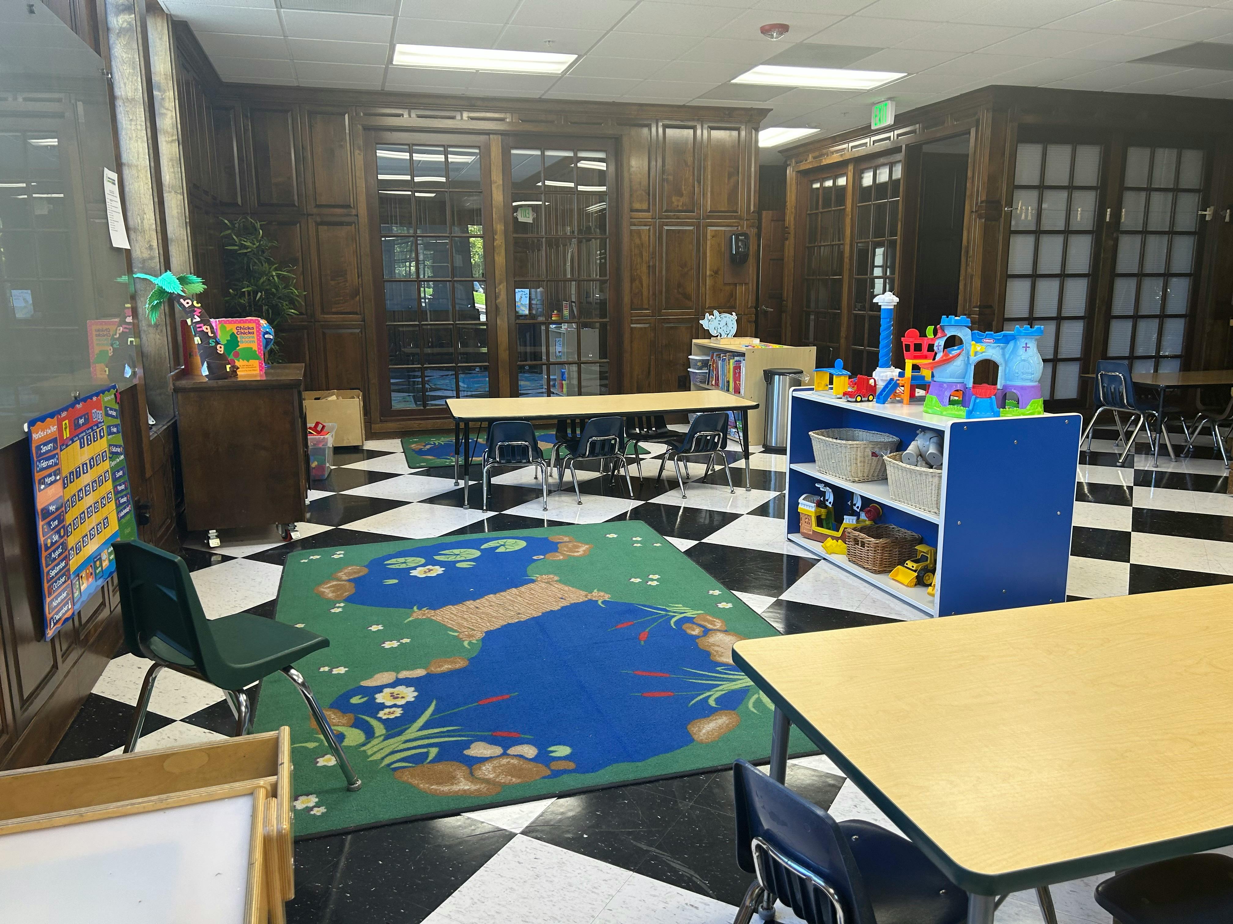 Classroom with small tables and chairs, a blue and green rug, and toys