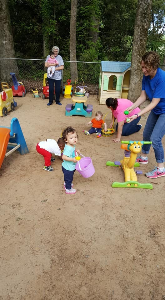 People and children playing in a sandy outdoor area with toys