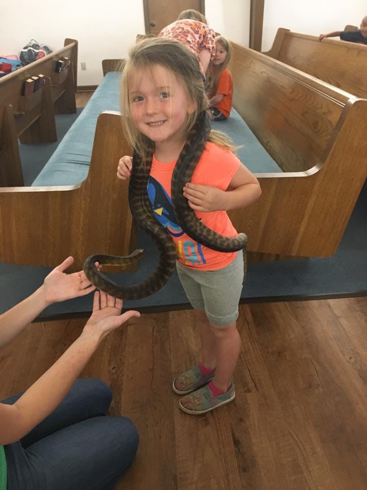 Child with a snake around their neck, another person reaching out