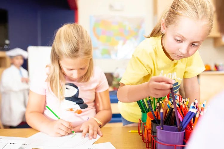 Two children drawing and selecting art supplies in a classroom