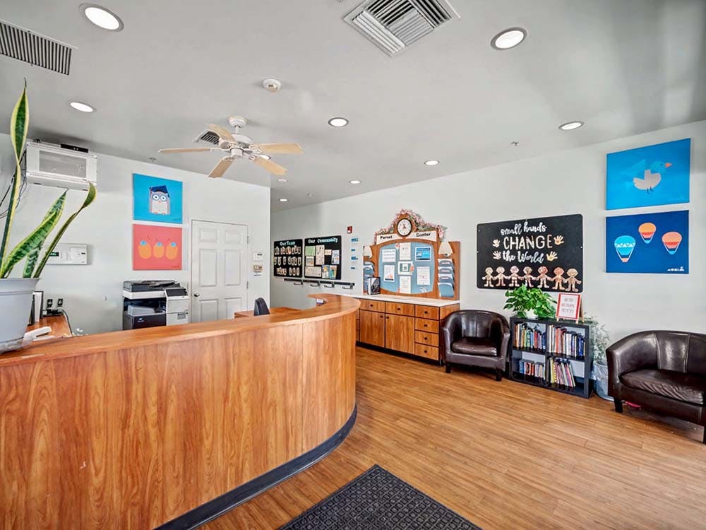 Reception area with a wooden desk, two brown chairs, and art on the walls