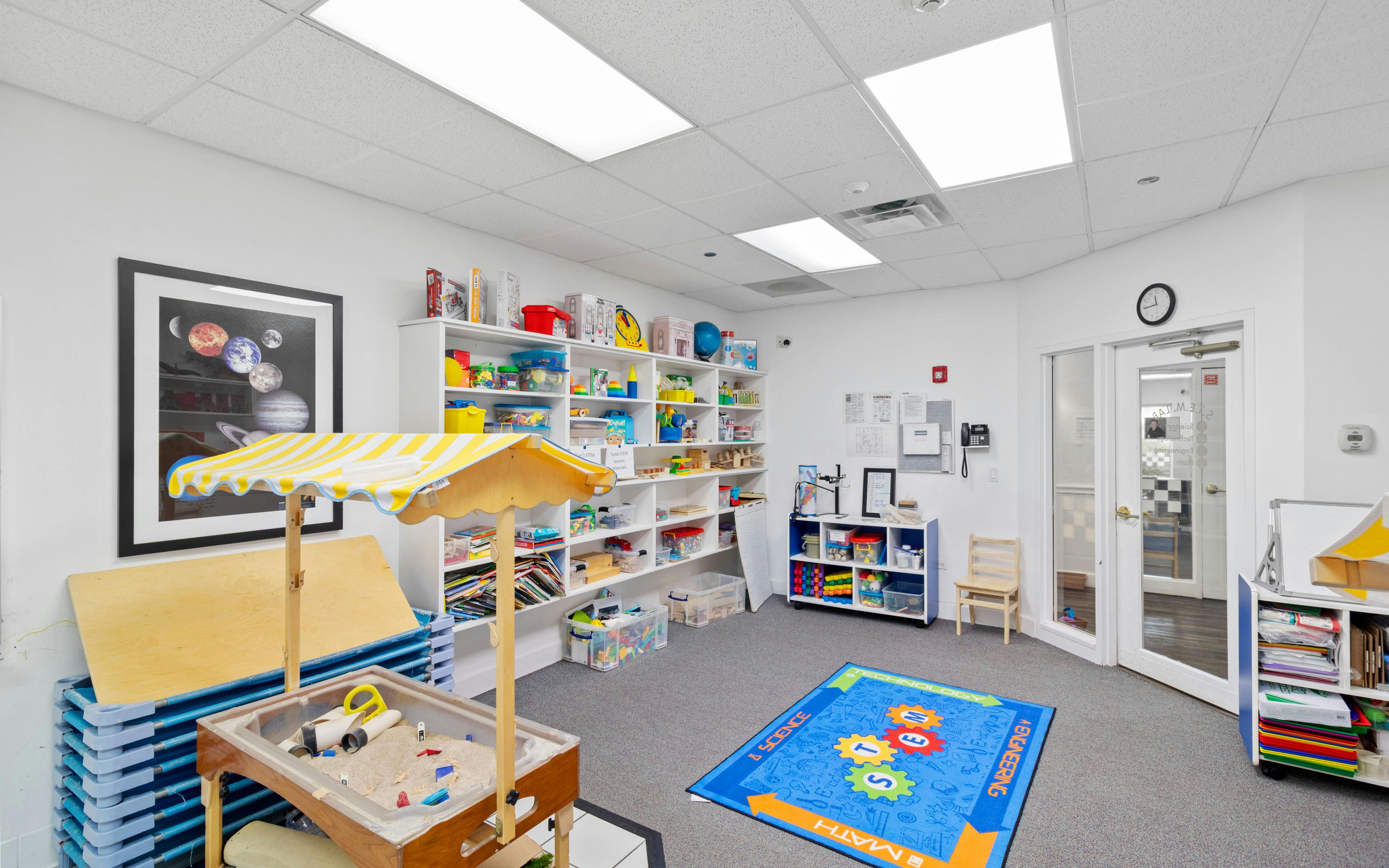 Classroom with shelves of toys, a sand and water table, and a blue rug