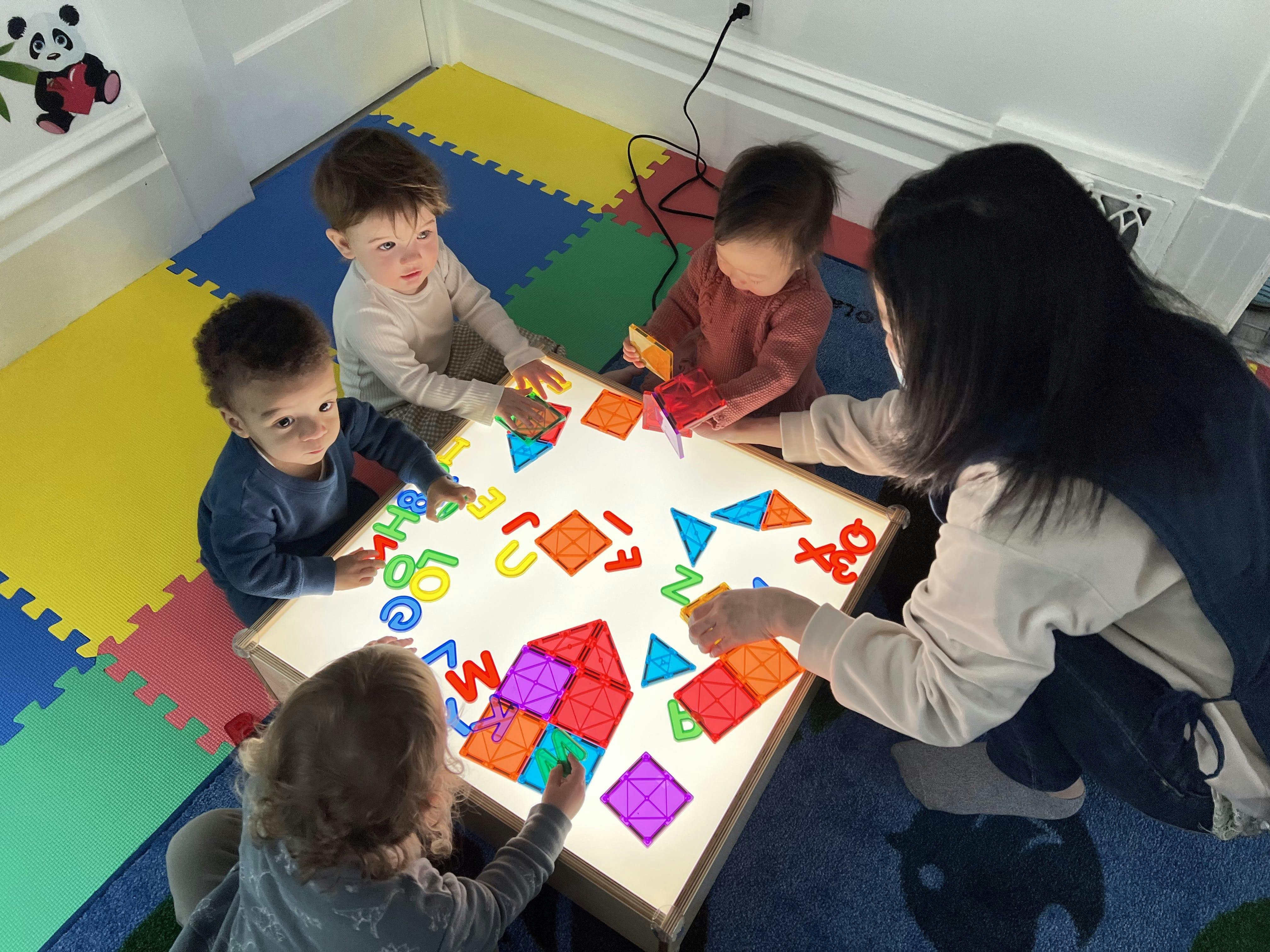 Adult and children playing with colorful shapes and letters on a light table