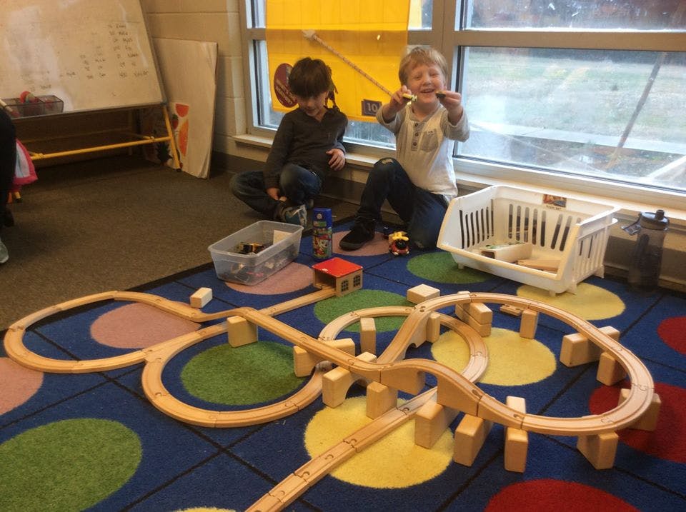 Two children playing with a wooden train set on a colorful rug