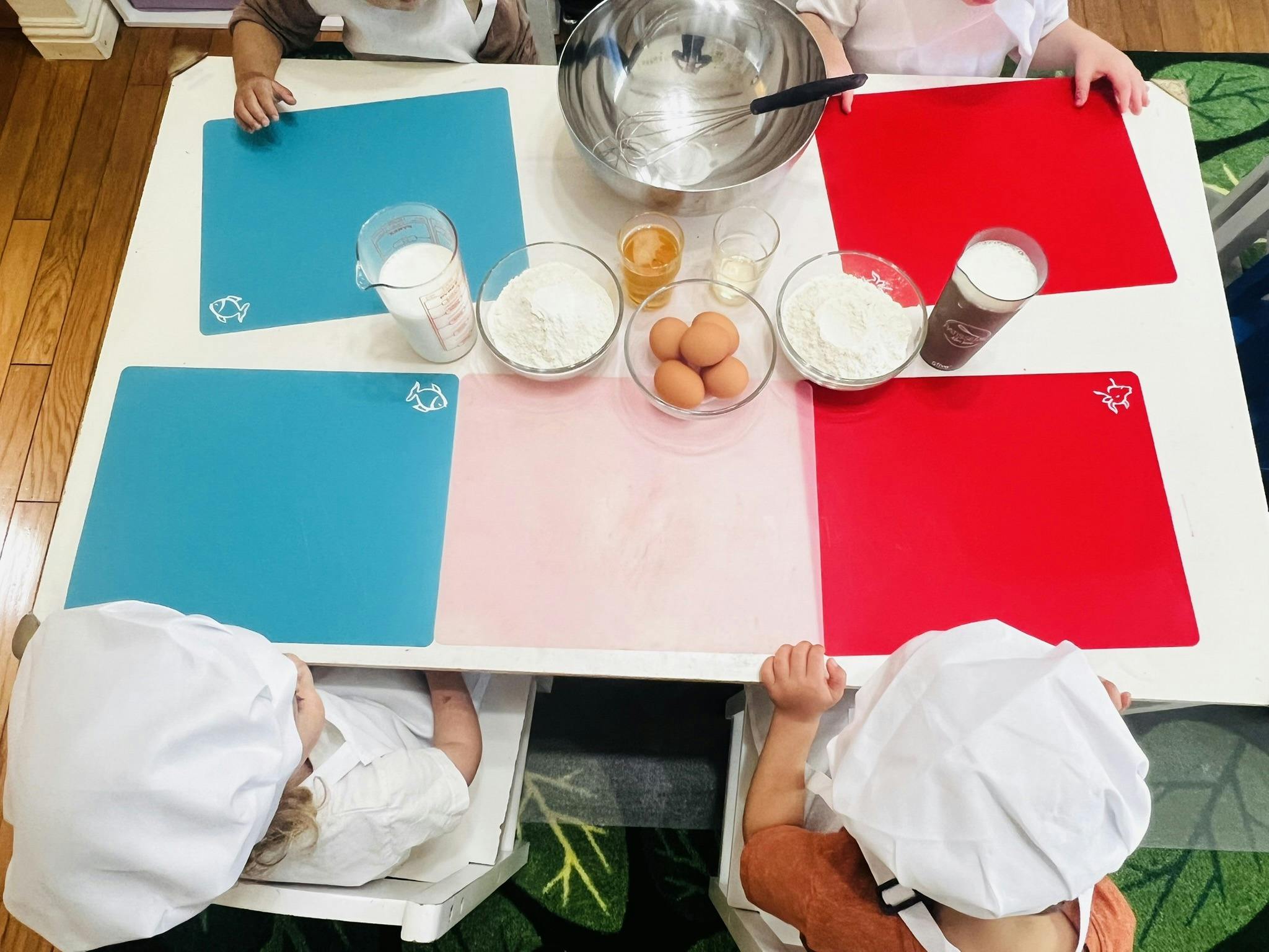 Several children in chef hats and aprons at a table with baking ingredients