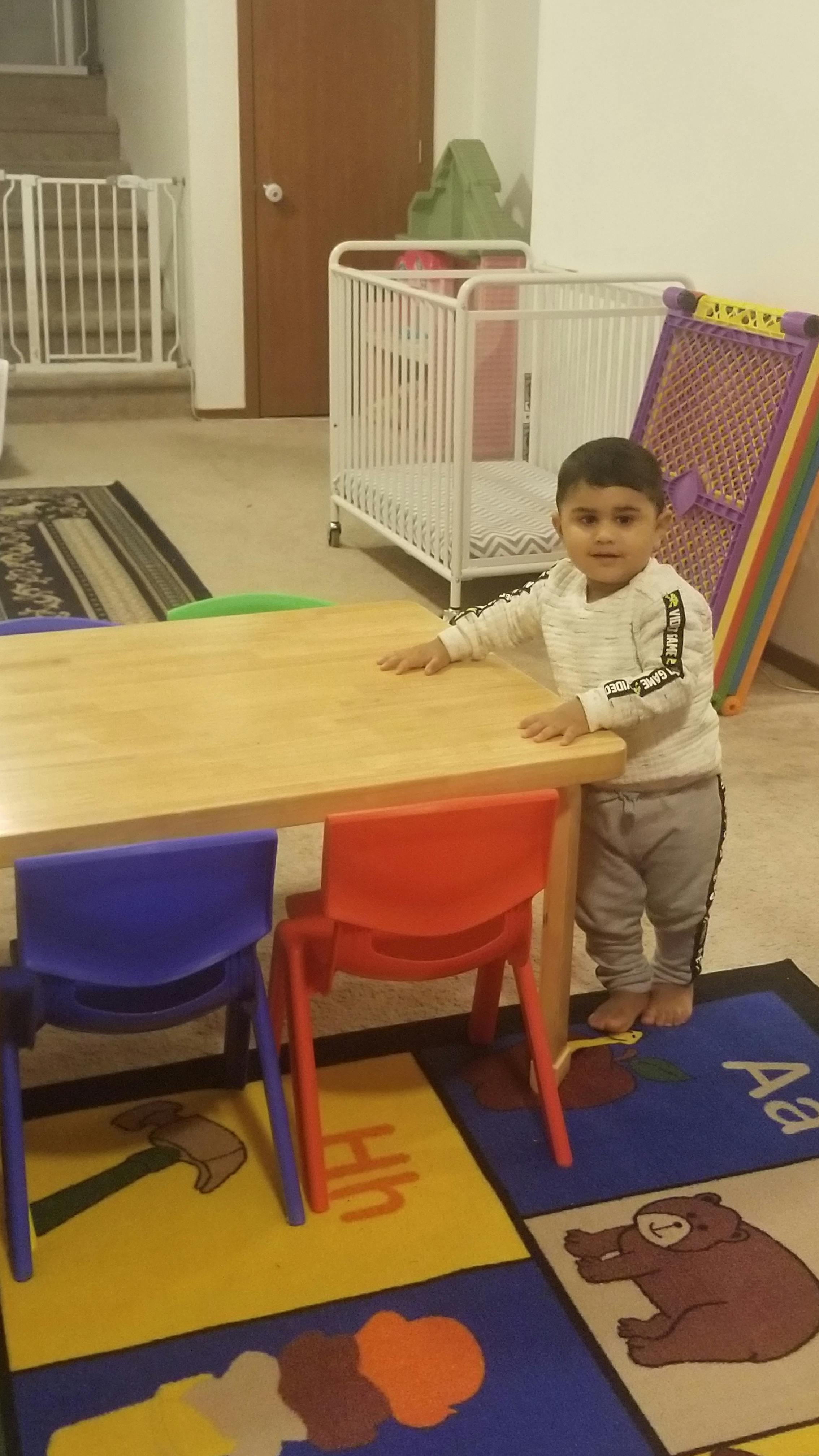 Child standing next to a small wooden table with two chairs