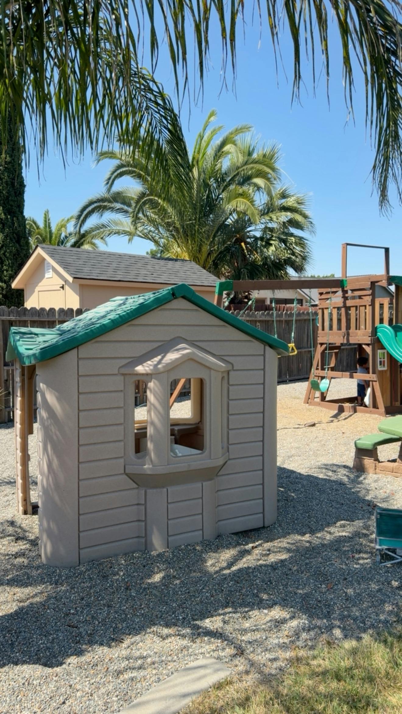 Plastic playhouse and wooden playset in a backyard