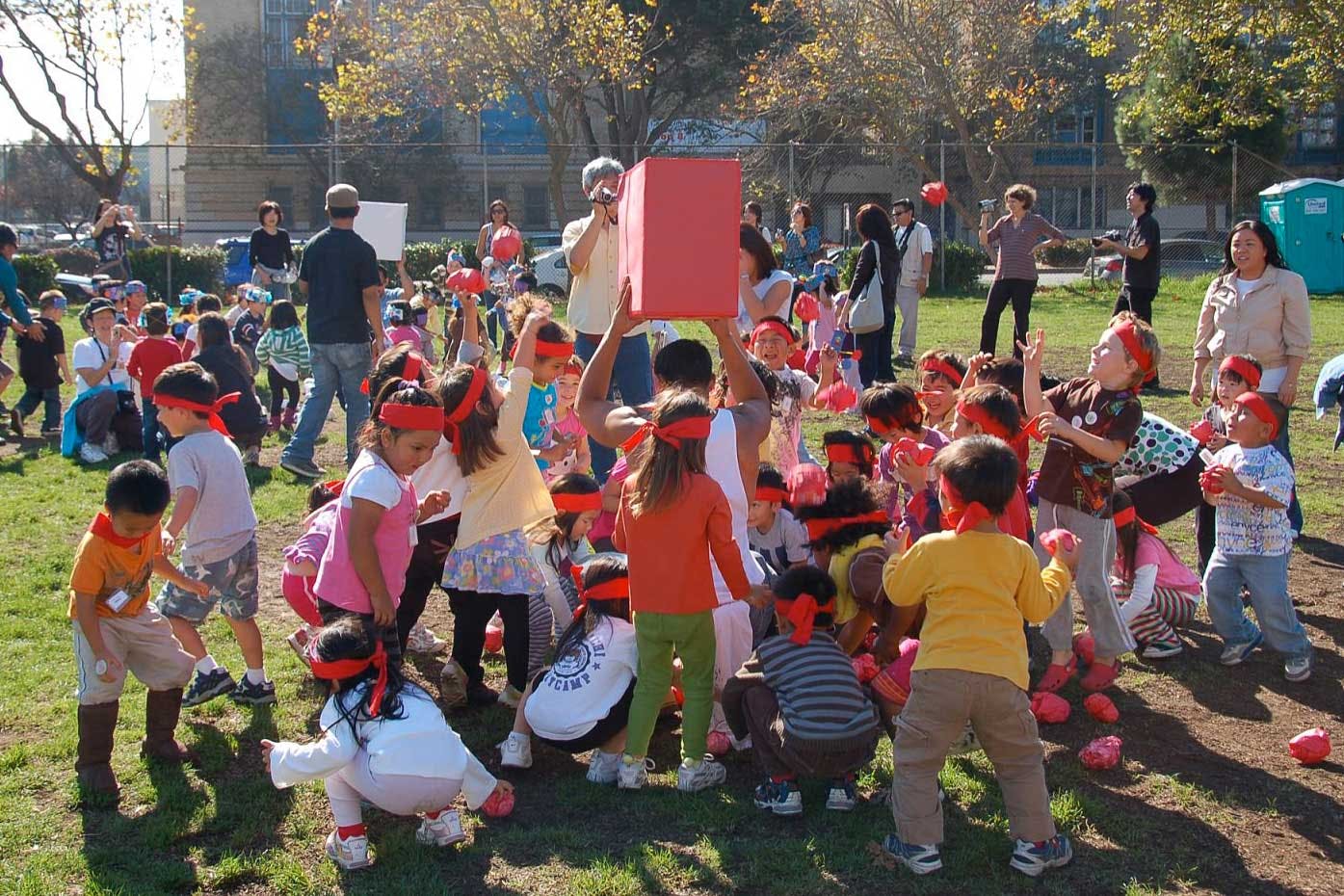 Many children and adults gathered outdoors, some holding red objects