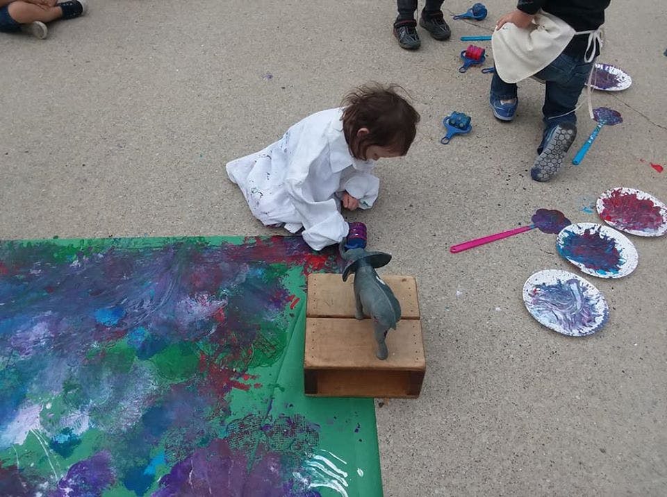 Child in white smock painting on a green canvas with a toy animal