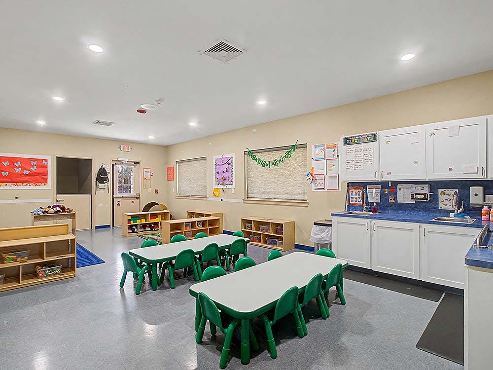 Classroom with small tables and chairs, shelves, and a sink area