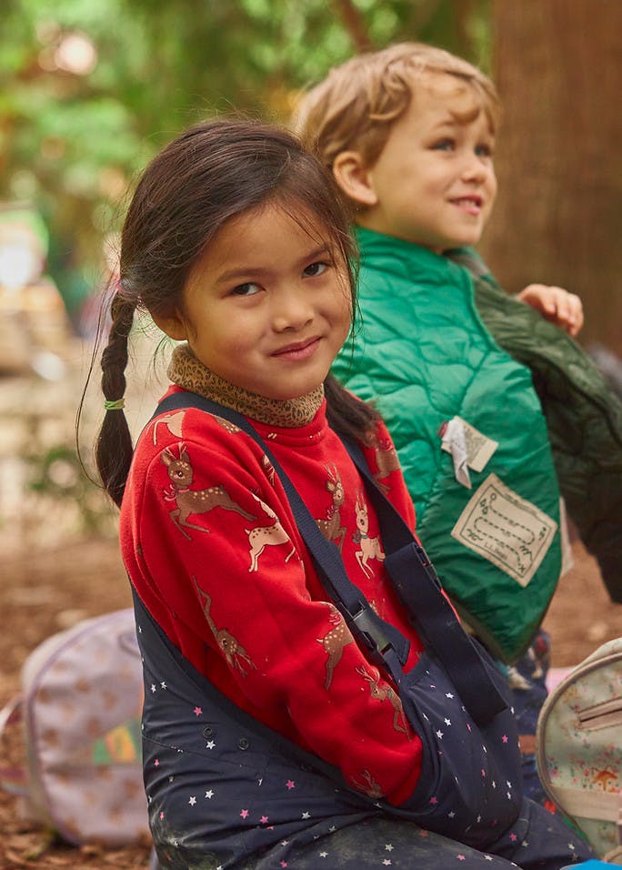 Child in red sweater with deer pattern and another child in green jacket