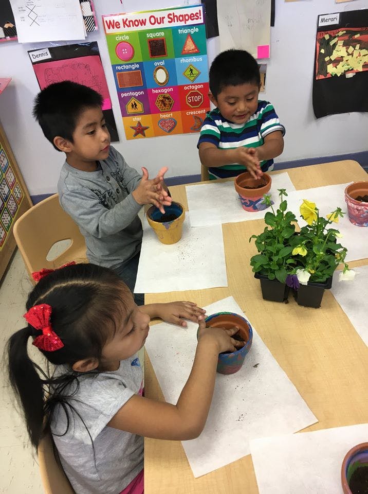 Three children planting in pots at a table