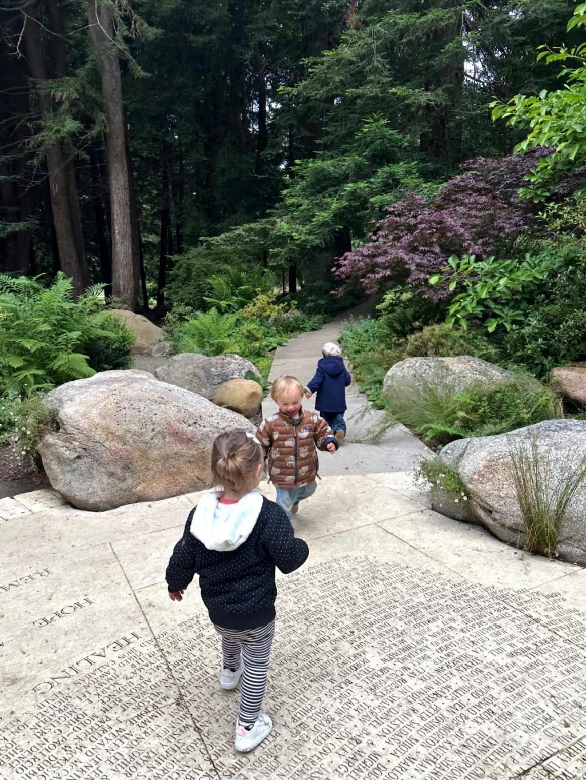 Three children walking on a stone path engraved with names in a garden