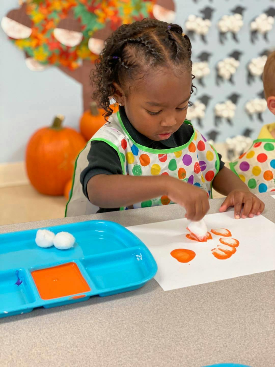 Child painting with orange paint and cotton balls