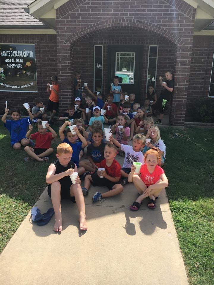 Group of children sitting outside a building, holding cups