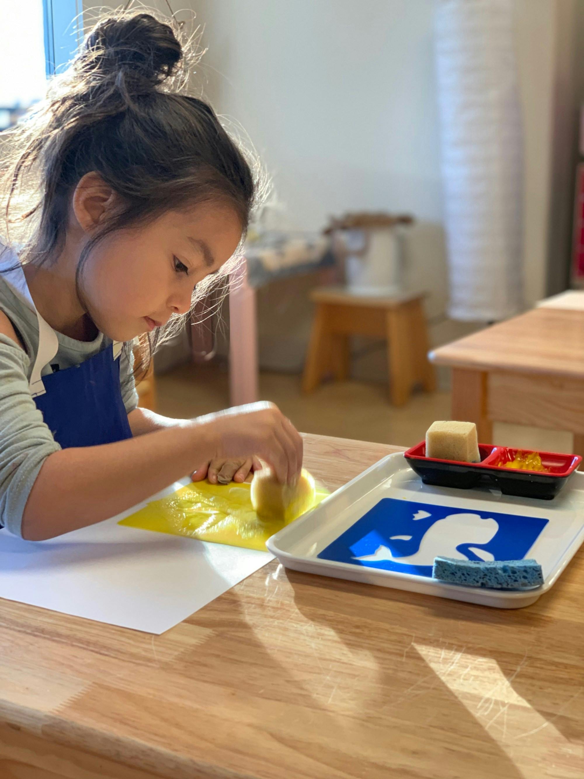 Child using a sponge to apply paint to paper