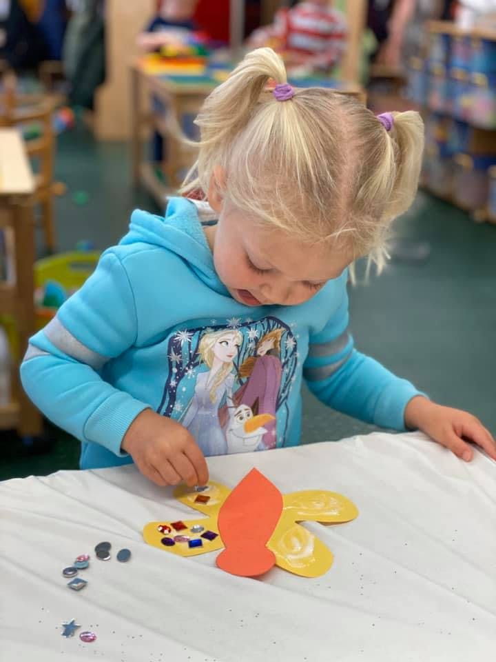 Child decorating a paper butterfly with small colorful pieces
