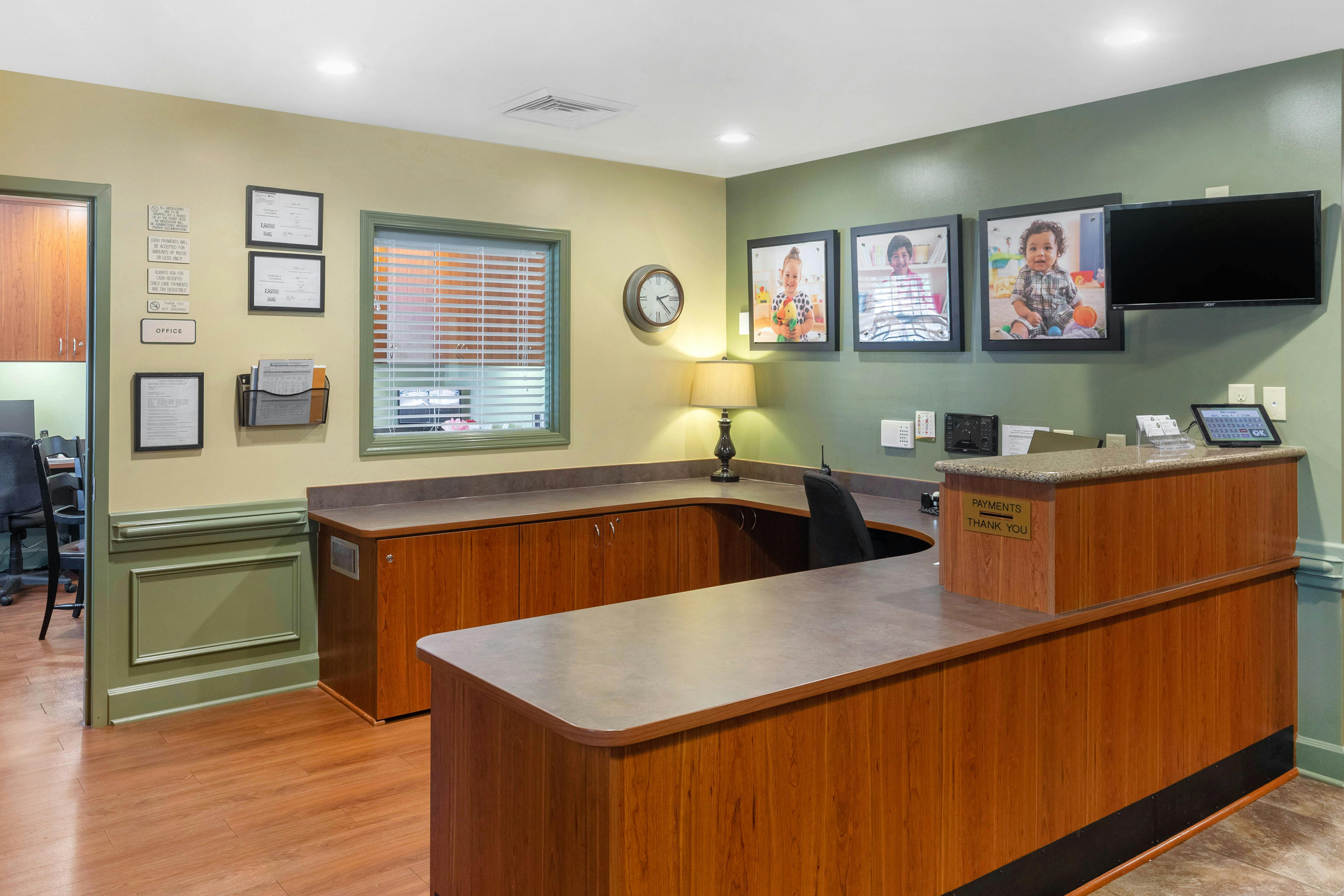Reception desk with office door, three framed photos of children, and a payment sign