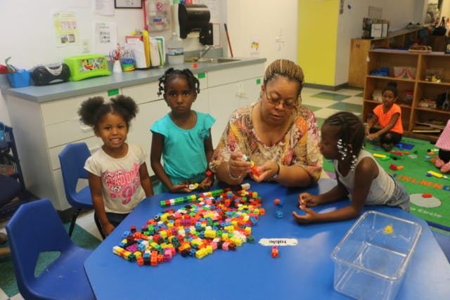 Person and three children playing with colorful building blocks at a table
