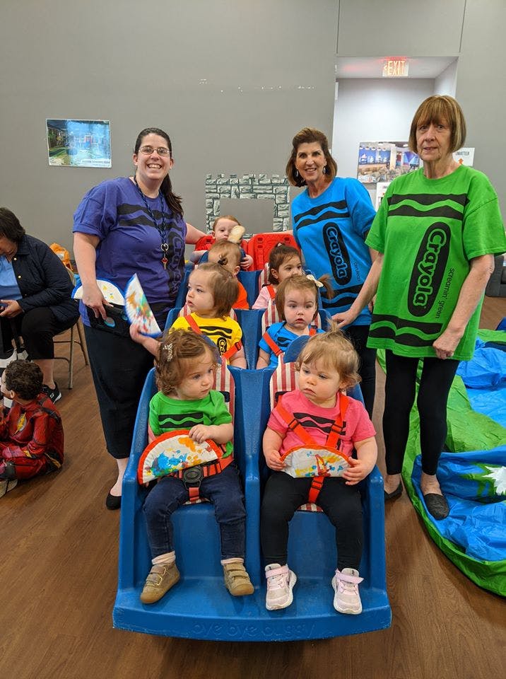 Three adults and multiple children, some seated in blue chairs