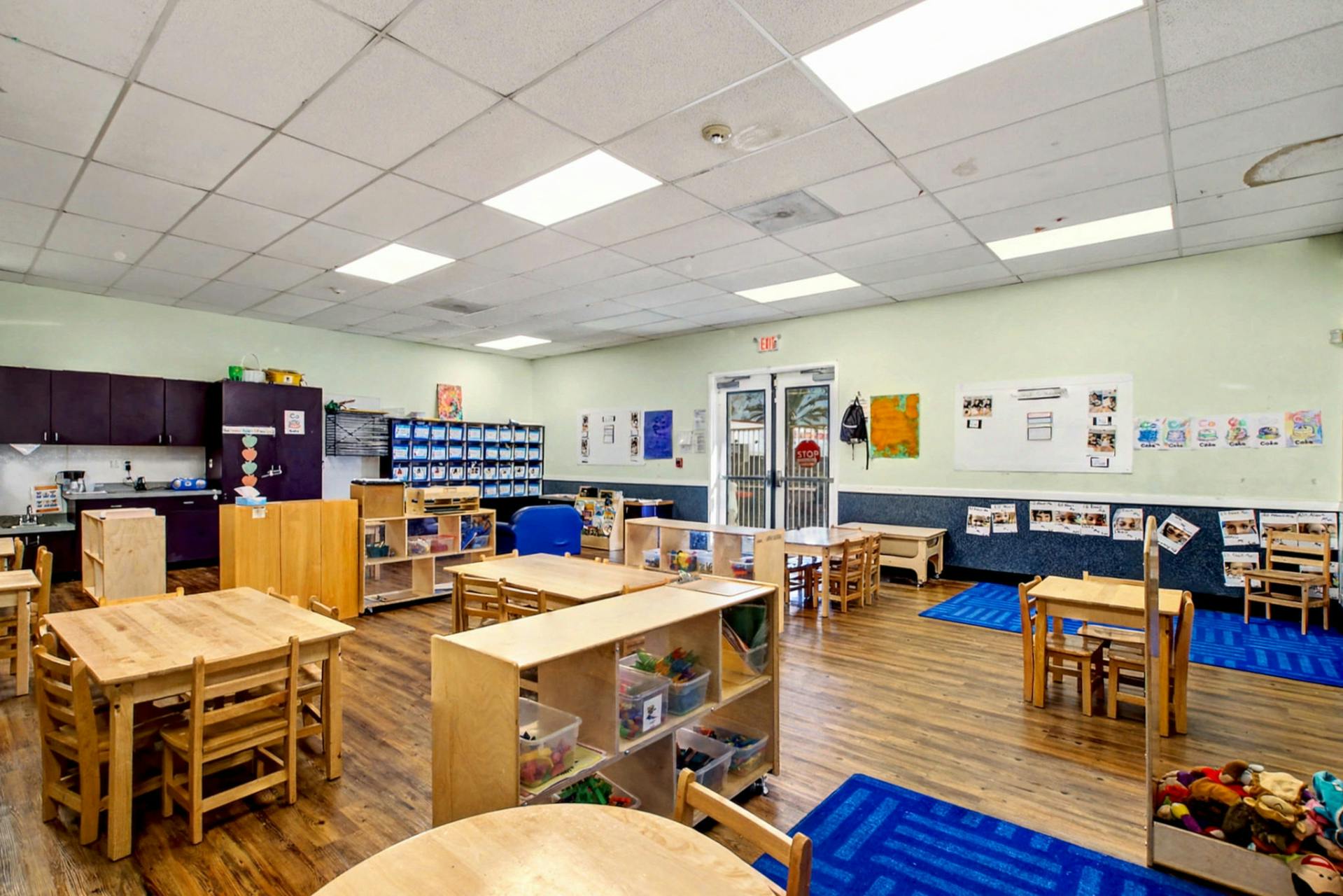 Classroom with small wooden tables and chairs, and shelving units
