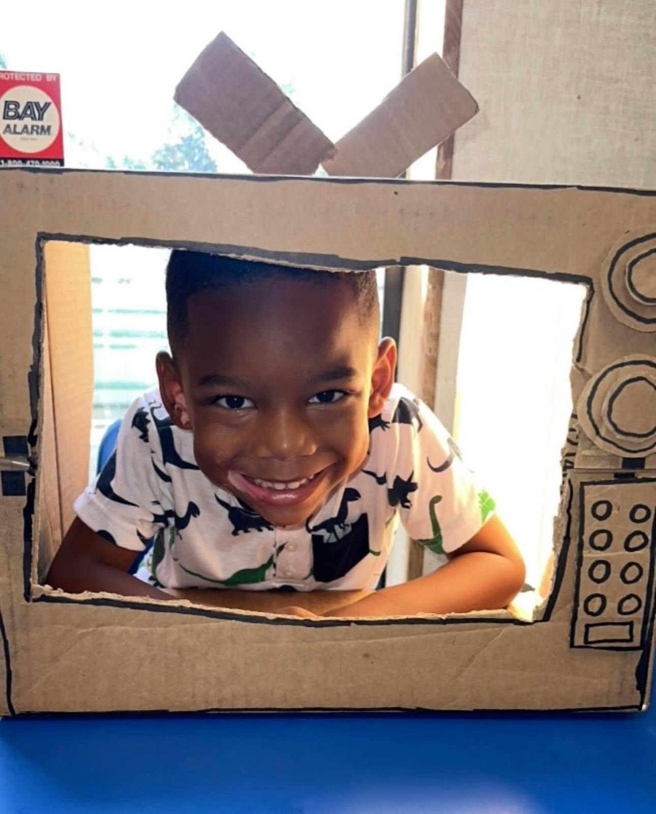 Child peeking through a cardboard box decorated to look like a television
