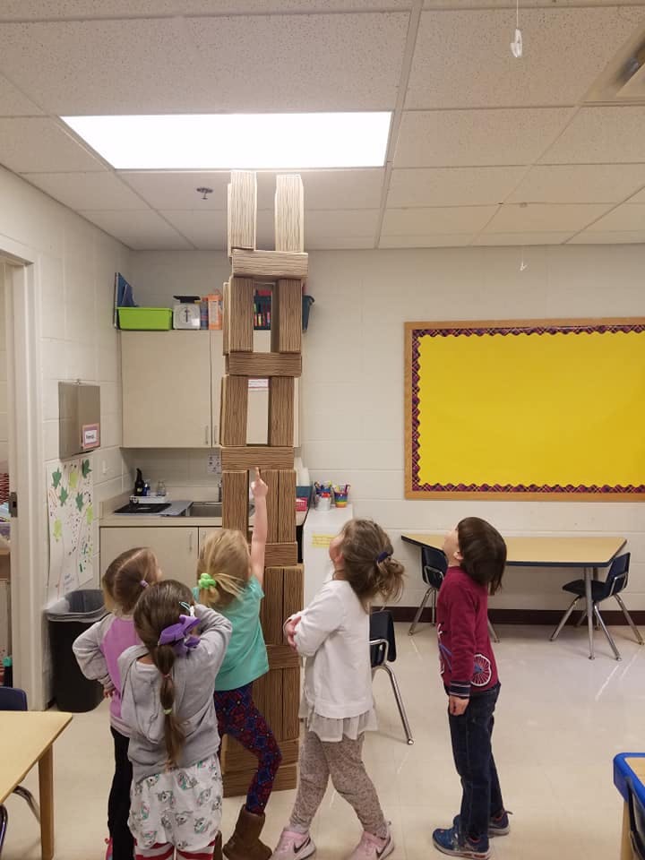 Children looking up at a tall tower of blocks in a classroom