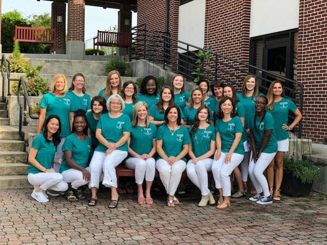 Group of people in matching teal shirts and white pants posing outdoors