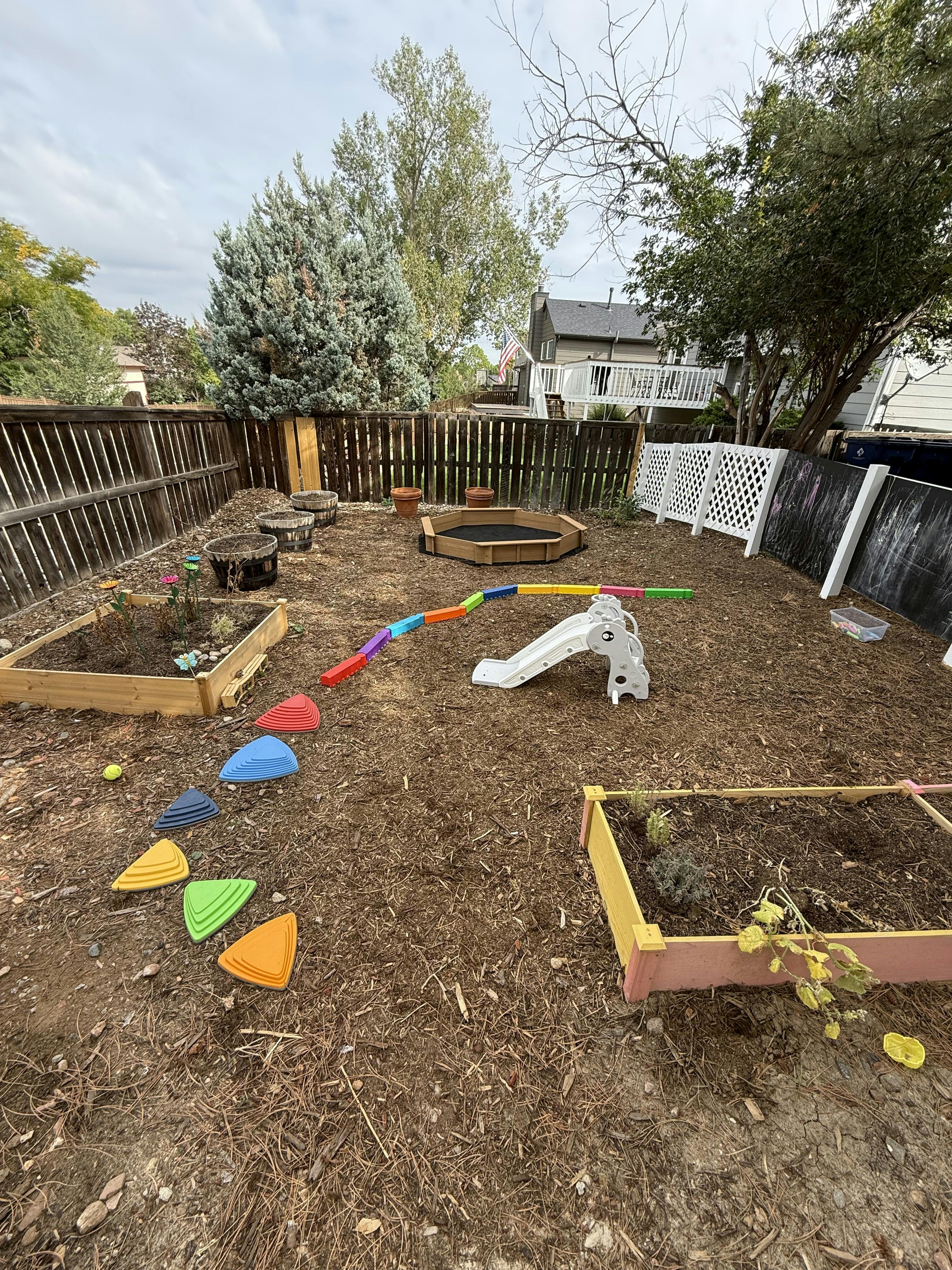 Backyard play area with raised garden beds, a small slide, and balance equipment