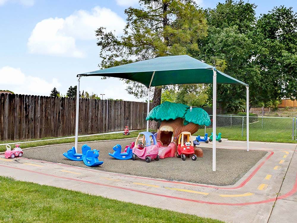 Outdoor play area with ride-on toys, rockers, and a playhouse under a shade cover
