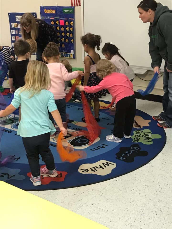 Adults and children playing with colorful scarves in a classroom