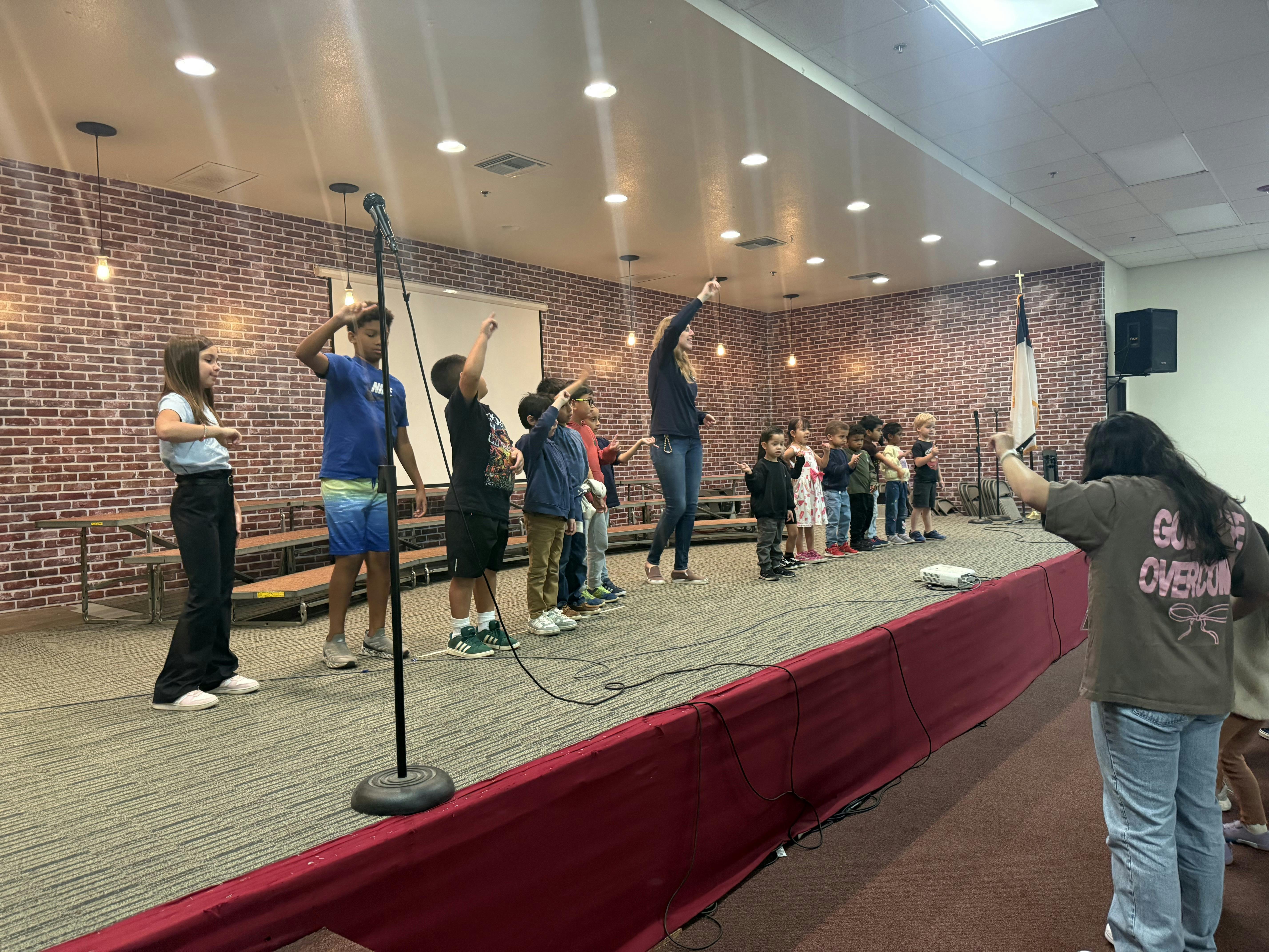 Group of children and adults on a stage with hands raised